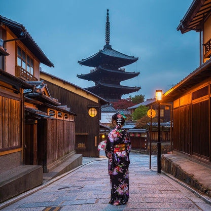 Woman in a traditional kimono standing in a Japanese street with wooden buildings and a pagoda in the background.